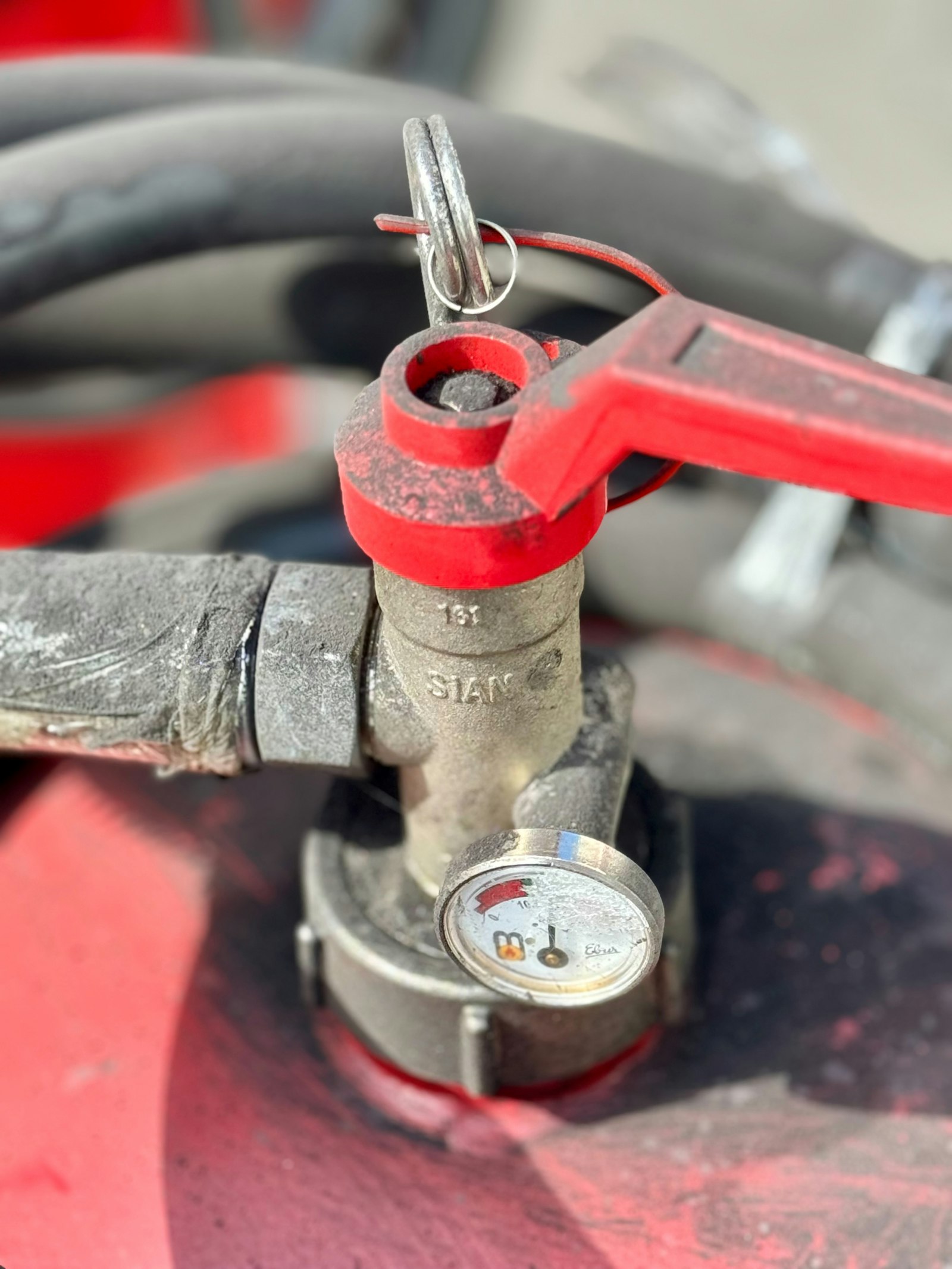 Close-up of a red shut-off valve with a pressure gauge